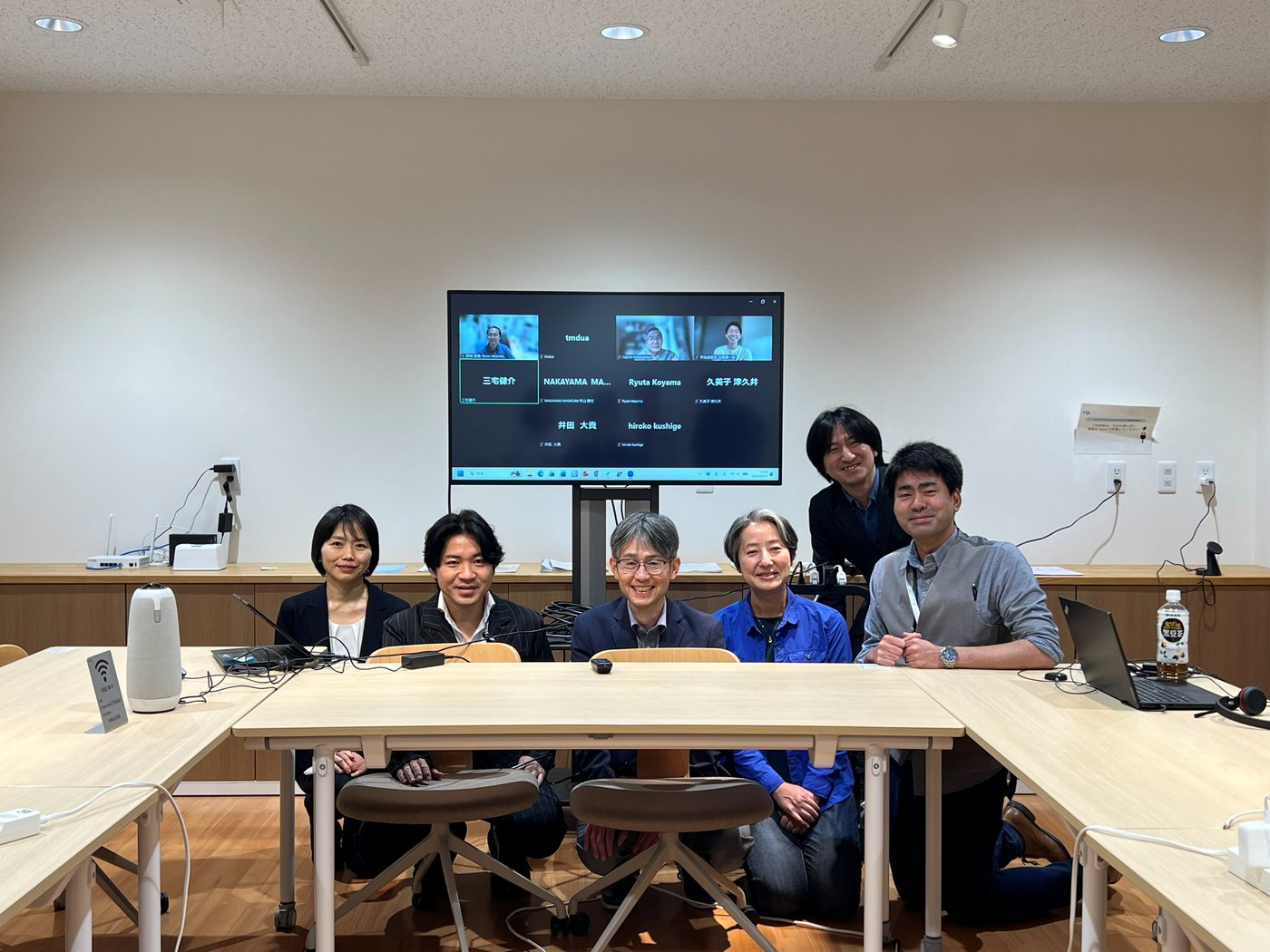 キックオフミーティングの会場風景。オンライン参加者を映したモニターを囲む参加者